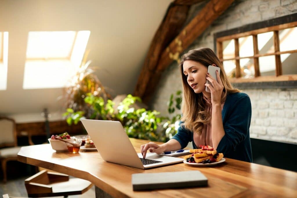 young businesswoman talking on the phone while using computer at home